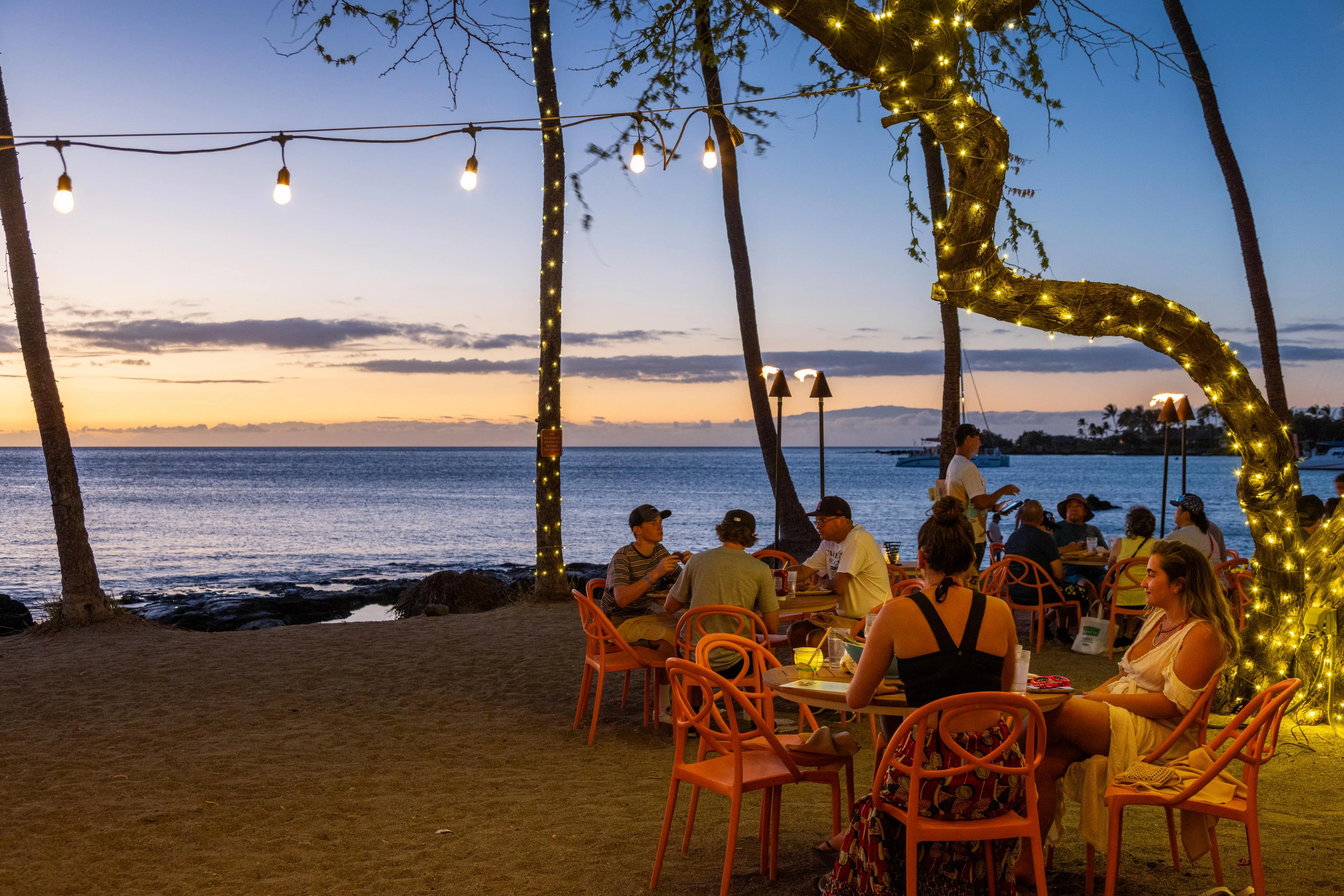Beachfront tables strung with lights as the sun sets over Anaeho'omalu Bay