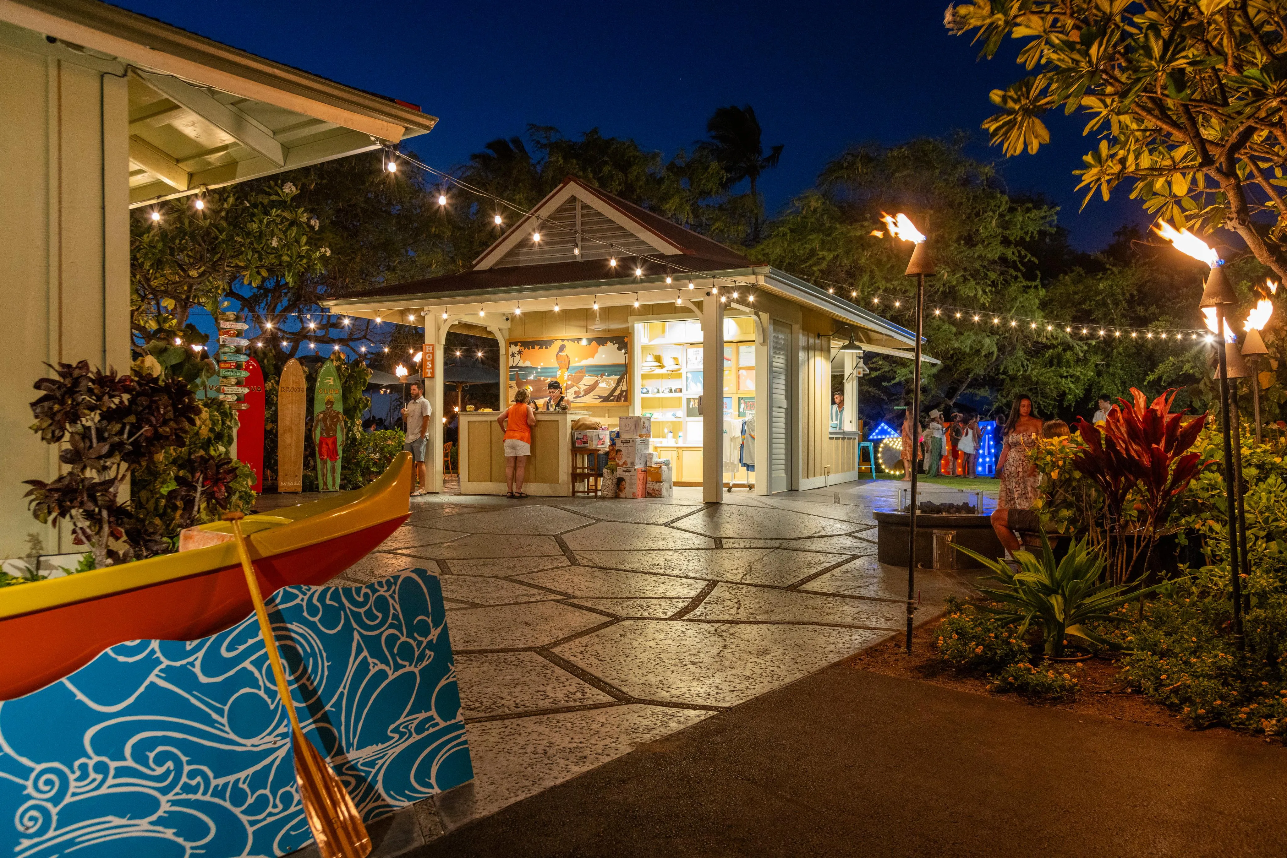 Lava Lava Beach Club lit up at night with string lights and its outrigger-canoe mural