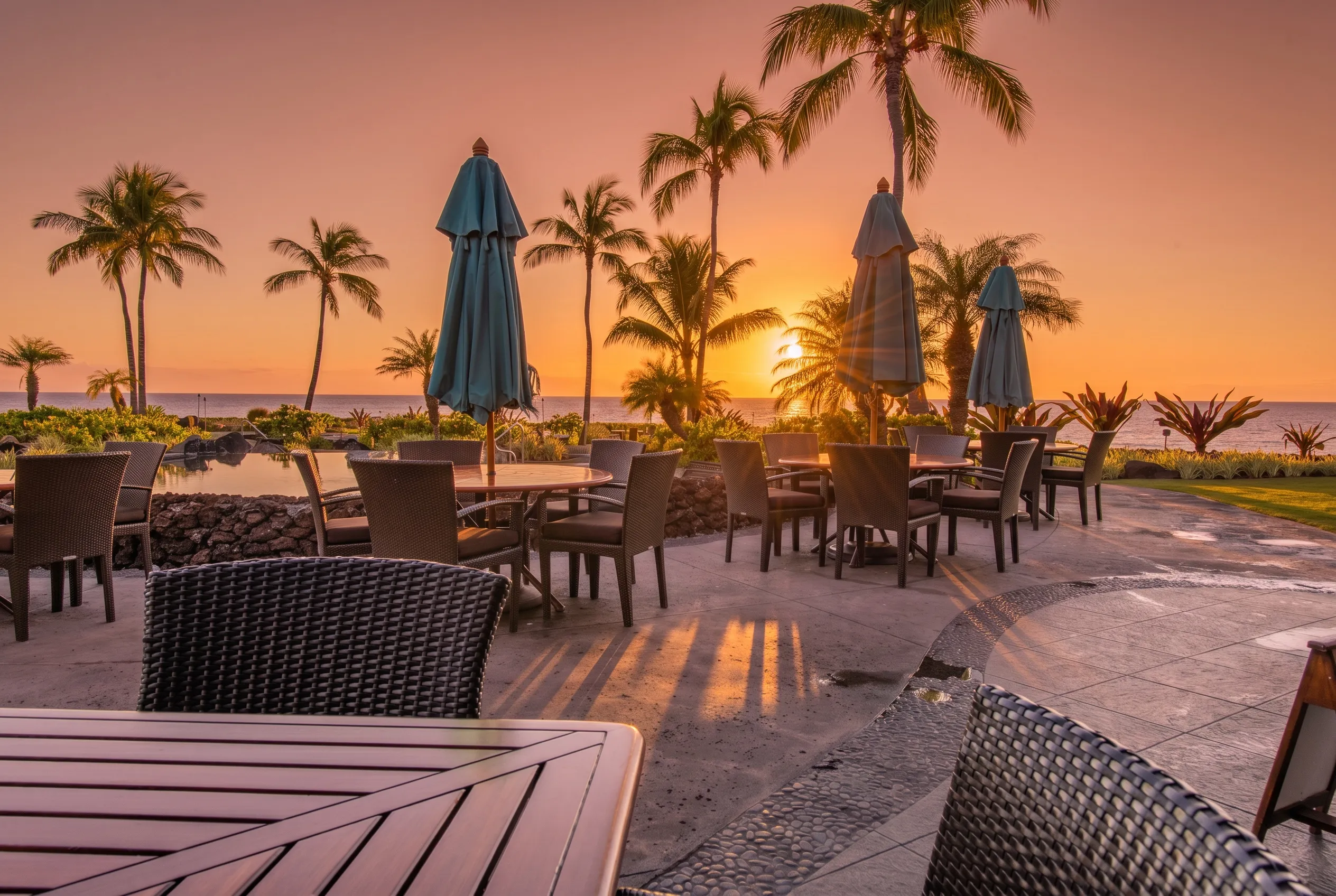 The Ocean Club's oceanfront patio tables and pool at sunset, palms silhouetted against the Pacific at Hali'i Kai