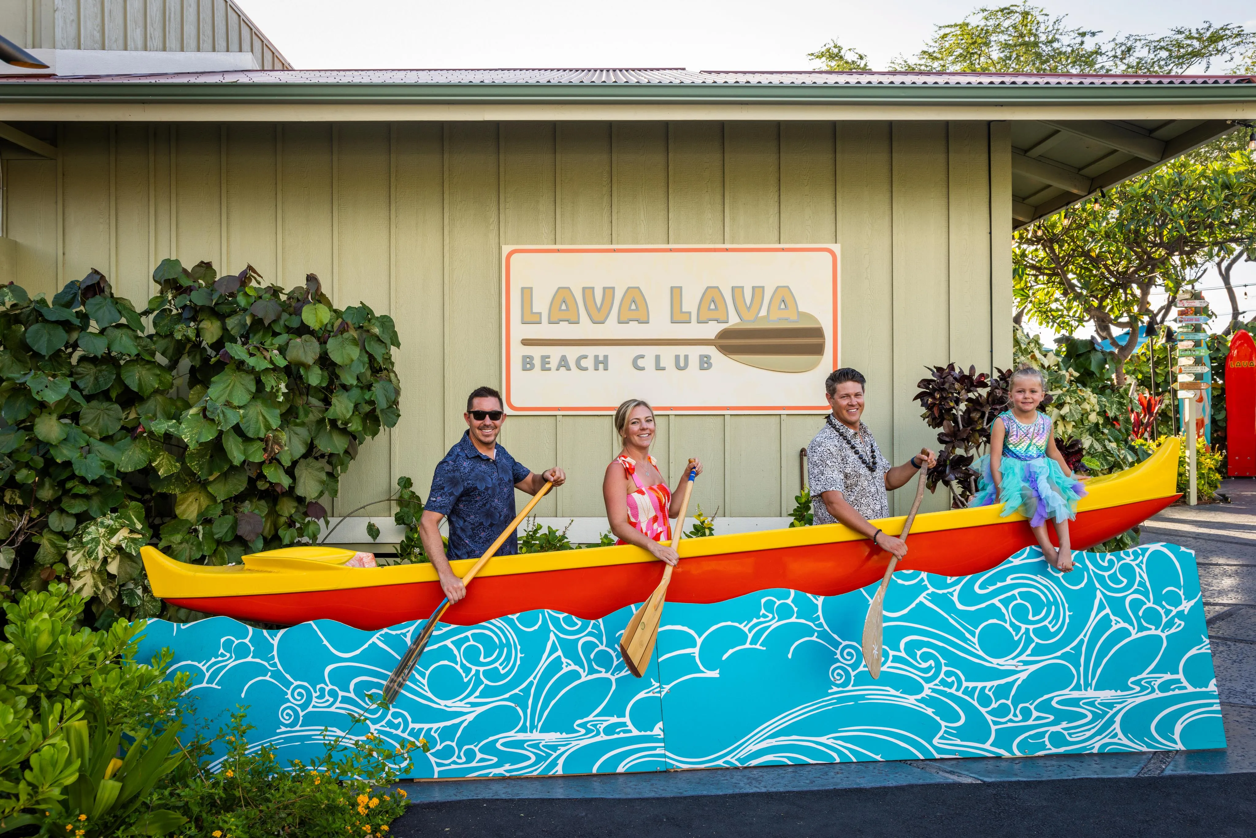 Guests at the Lava Lava Beach Club sign beside its painted outrigger canoe